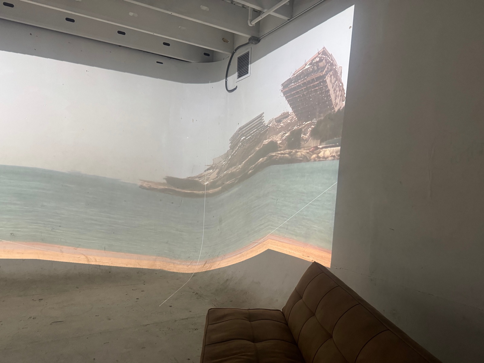 A projection of water and a tilted architectural structure spans the corner of the installation room.