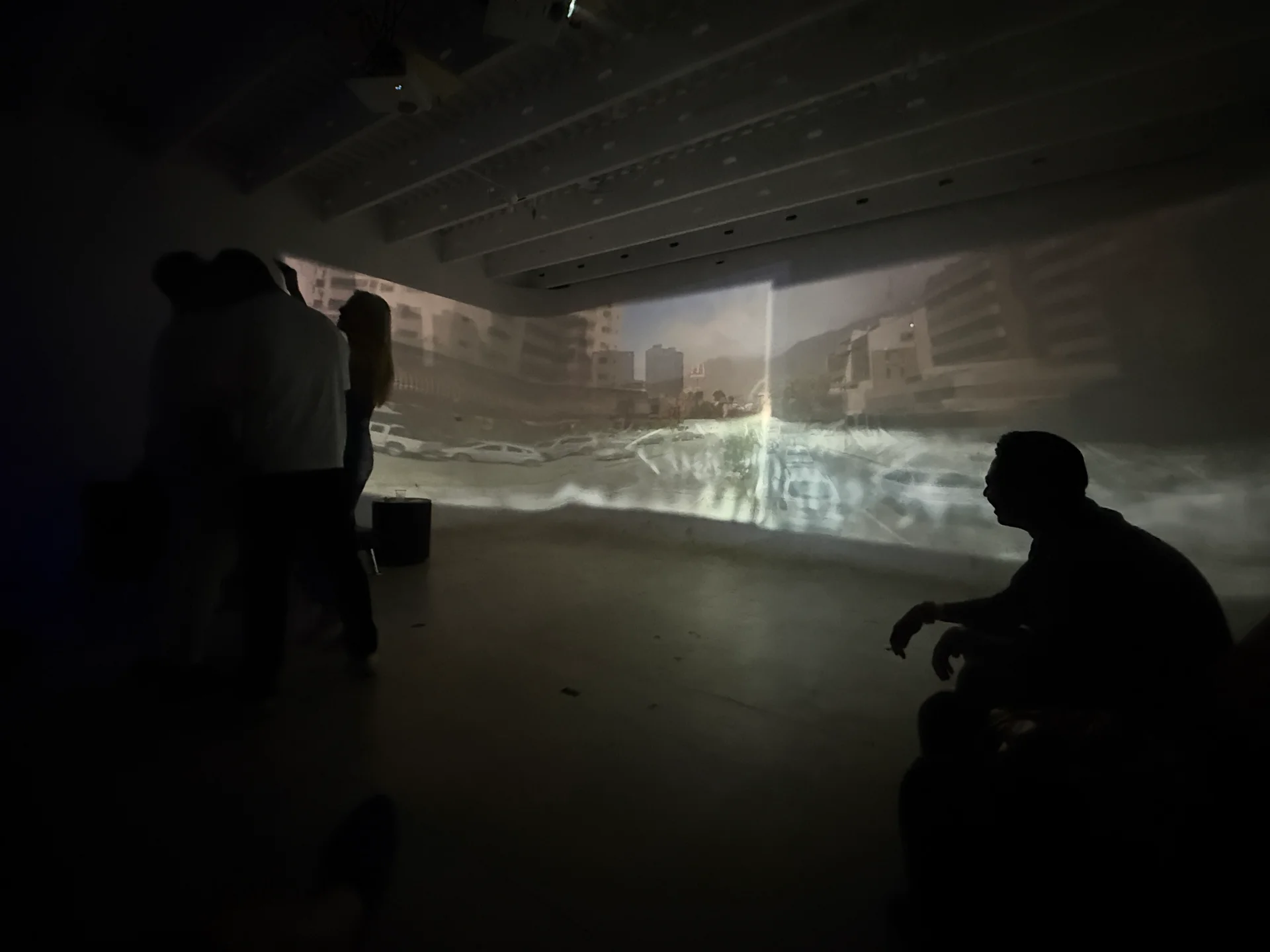 Visitors stand and sit inside Coast Echoes as images of buildings and water stretch across adjoining walls.